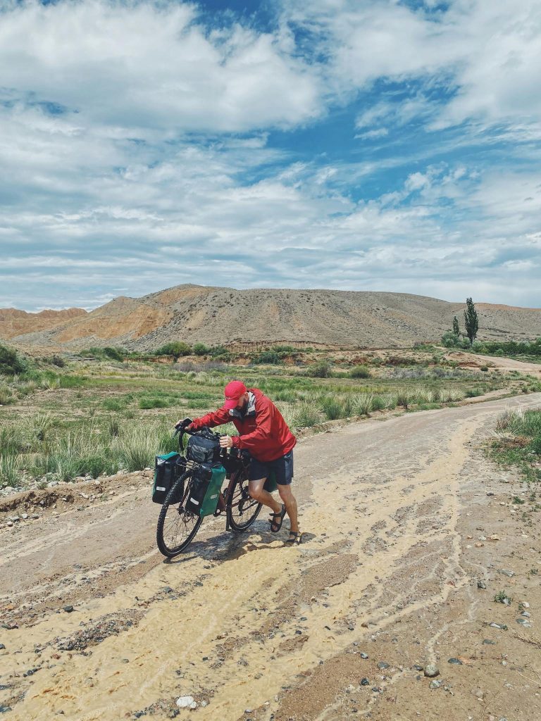 A cyclist pushes their bike across a rugged desert path under a cloudy sky, embracing adventure.